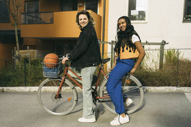 Porträt von lächelnden Freundinnen auf dem Fahrrad sitzend vor einem Gebäude am Fußweg - MASF38030