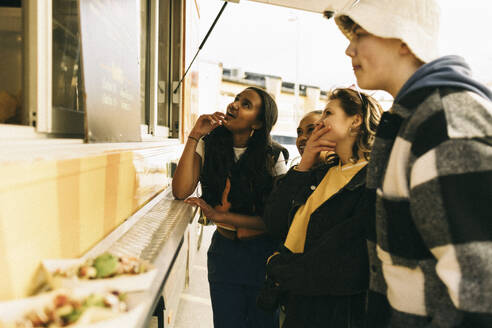 Male and female friends choosing food from menu while standing near concession stand - MASF38036