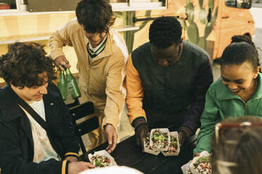 High angle view of happy friends arranging food boxes on table - MASF38038