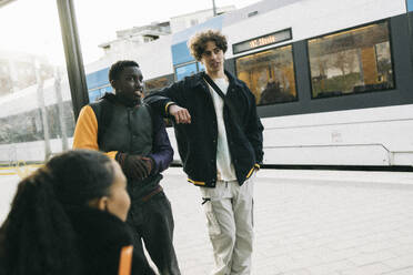 Teenage boy discussing with male friend while waiting at train station - MASF38046