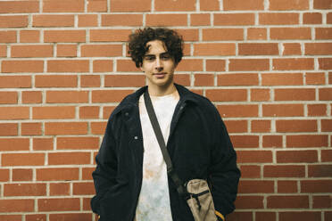 Portrait of teenage boy wearing jacket while standing against brick wall - MASF38054