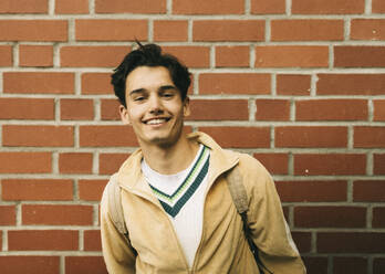 Portrait of smiling young man against brick wall - MASF38056