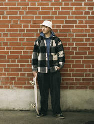 Young man with skateboard posing in front of brick wall - MASF38057