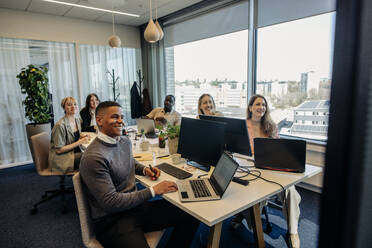 Lächelnde männliche und weibliche Geschäftskollegen während einer Videokonferenz in einem Coworking-Büro - MASF38088