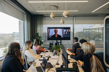 Geschäftsfrau, die ein Videogespräch mit einem männlichen und einem weiblichen Kollegen führt, die an einem Schreibtisch in einem Coworking-Büro sitzen - MASF38091