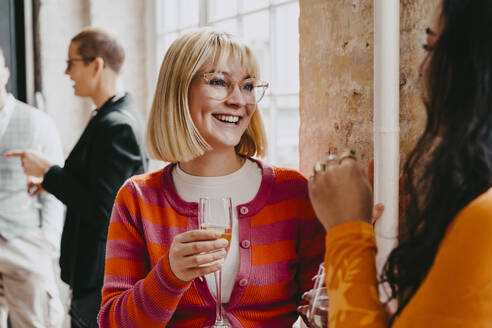 Glückliche blonde Geschäftsfrau genießt ein Getränk mit einer Kollegin während einer Veranstaltung im Kongresszentrum - MASF38095