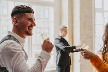 Side view of smiling businessman drinking white wine during event at convention center - MASF38106