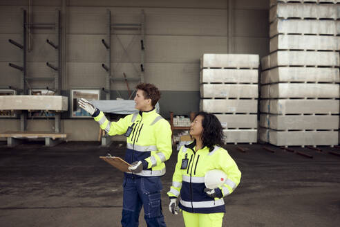 Female workers in protective workwear discussing at warehouse - MASF38189