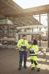 Happy female workers in protective workwear discussing while standing at warehouse - MASF38190