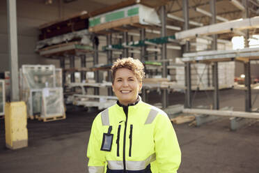 Portrait of smiling female worker standing in front of distribution warehouse - MASF38193