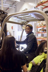 Lächelnde Gabelstaplerfahrerin im Gespräch mit einem Mitarbeiter in einem Vertriebslager - MASF38217