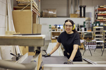 Porträt einer lächelnden Schreinerin, die bei ihrer Arbeit in der Industrie eine Schutzbrille und einen Gehörschutz trägt - MASF38224