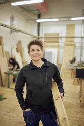 Porträt einer selbstbewussten reifen Schreinerin, die in der Werkstatt stehend eine Planke trägt - MASF38232