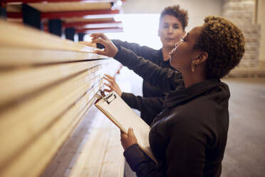 Multiracial female colleagues examining planks on rack in lumber industry - MASF38241