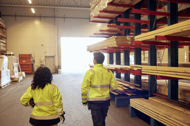 Rear view of female workers in protective workwear walking by rack in lumber industry - MASF38243