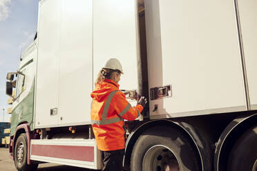 Female worker locking door of truck outside factory on sunny day - MASF38245