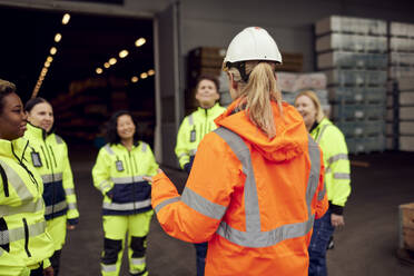 Rear view of female engineer in reflective clothing discussing with workers at industry - MASF38248