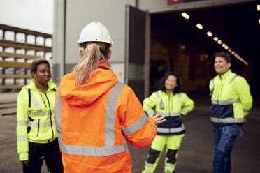 Rear view of female engineer in protective workwear discussing with workers at factory - MASF38249