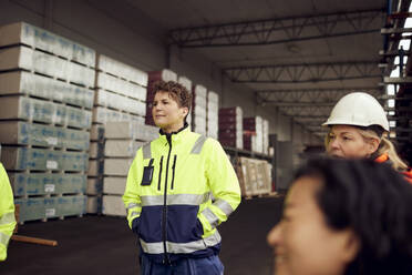Female engineer in reflective clothing standing with hands in pockets at factory - MASF38252