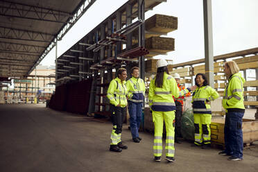 Female engineer discussing with multiracial colleagues while standing at lumber industry - MASF38254