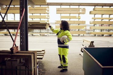 Side view of female worker examining planks stacked at lumber industry - MASF38274