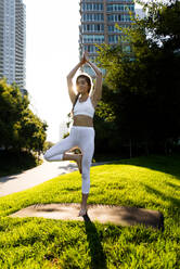 Beautiful sportive woman doing yoga meditation in a park - Girl relaxing with serene expression outdoors - DMDF03326