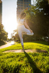 Beautiful sportive woman doing yoga meditation in a park - Girl relaxing with serene expression outdoors - DMDF03328
