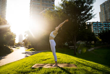 Beautiful sportive woman doing yoga meditation in a park - Girl relaxing with serene expression outdoors - DMDF03330