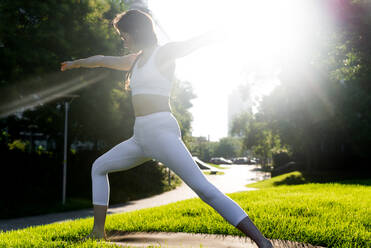 Beautiful sportive woman doing yoga meditation in a park - Girl relaxing with serene expression outdoors - DMDF03337