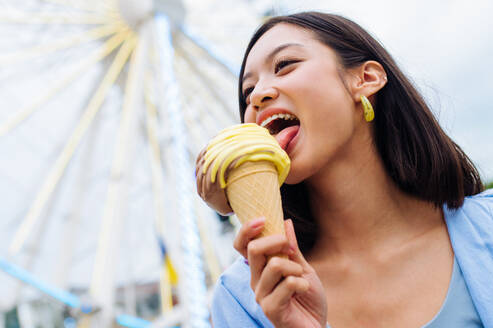 Schöne junge asiatische Frau isst Eis im Vergnügungspark - Fröhliches chinesisches Frauenporträt im Sommerurlaub - Freizeit, Menschen und Lifestyle-Konzepte - DMDF03443