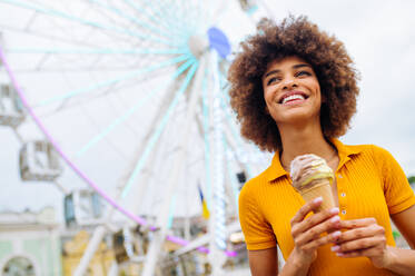 Schöne junge schwarze Frau isst Eis im Vergnügungspark - Fröhliches afrikanisch-amerikanisches Frauenporträt während der Sommerferien - Freizeit-, Menschen- und Lifestyle-Konzepte - DMDF03445