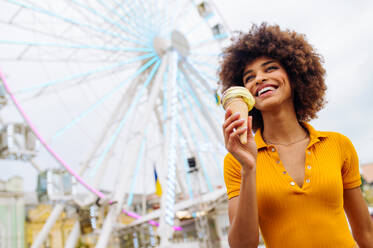 Schöne junge schwarze Frau isst Eis im Vergnügungspark - Fröhliches afrikanisch-amerikanisches Frauenporträt während der Sommerferien - Freizeit-, Menschen- und Lifestyle-Konzepte - DMDF03446