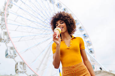 Schöne junge schwarze Frau isst Eis im Vergnügungspark - Fröhliches afrikanisch-amerikanisches Frauenporträt während der Sommerferien - Freizeit-, Menschen- und Lifestyle-Konzepte - DMDF03448