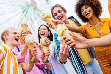 Gemischtrassige junge Leute, die sich in einem Freizeitpark treffen und Eis essen - Gruppe von Freunden mit gemischten Rassen, die Spaß im Freien haben - Freundschafts- und Lebensstilkonzepte - DMDF03449