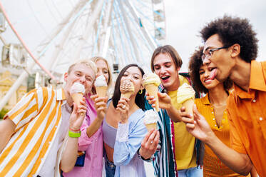 Gemischtrassige junge Leute, die sich in einem Freizeitpark treffen und Eis essen - Gruppe von Freunden mit gemischten Rassen, die Spaß im Freien haben - Freundschafts- und Lebensstilkonzepte - DMDF03450