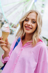 Beautiful young blond woman eating ice cream at amusement park - Cheerful caucasian female portrait during summertime vacation- Leisure, people and lifestyle concepts - DMDF03452