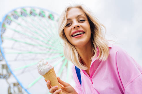 Schöne junge blonde Frau isst Eis im Vergnügungspark - Fröhliches kaukasisches Frauenporträt im Sommerurlaub - Freizeit-, Menschen- und Lebensstilkonzepte - DMDF03453