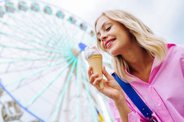 Beautiful young blond woman eating ice cream at amusement park - Cheerful caucasian female portrait during summertime vacation- Leisure, people and lifestyle concepts - DMDF03454