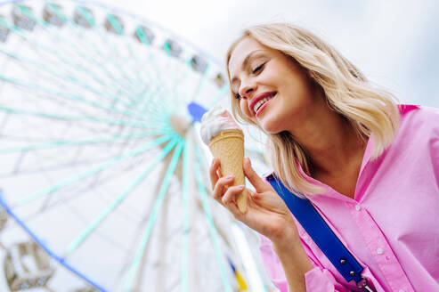 Schöne junge blonde Frau isst Eis im Vergnügungspark - Fröhliches kaukasisches Frauenporträt im Sommerurlaub - Freizeit-, Menschen- und Lebensstilkonzepte - DMDF03454