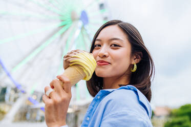 Schöne junge asiatische Frau isst Eis im Vergnügungspark - Fröhliches chinesisches Frauenporträt im Sommerurlaub - Freizeit, Menschen und Lifestyle-Konzepte - DMDF03457