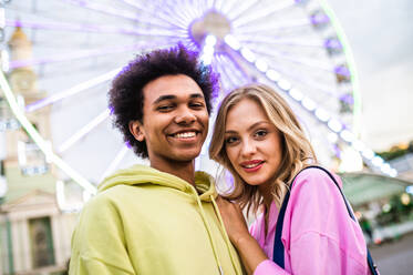 Multiracial young couple of lovers dating at theferry wheel in the amusement park - People with mixed races having fun outdoors in the city- Friendship, releationship and lifestyle concepts - DMDF03493