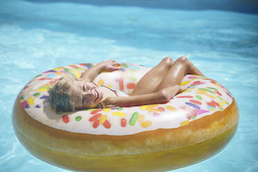 Lächelndes Mädchen entspannt sich mit aufblasbarem Krapfen im Schwimmbad - NJAF00559