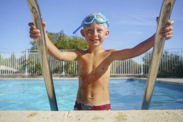 Lächelnder Junge, der an einem sonnigen Tag aus dem Schwimmbad steigt - NJAF00563