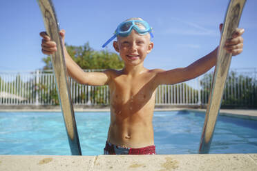 Smiling boy getting out of swimming pool on sunny day - NJAF00563