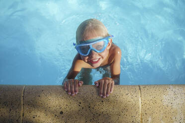 Cute boy with swimming goggles playing in pool - NJAF00565