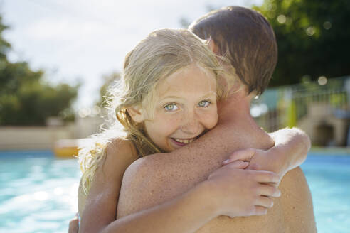 Lächelndes blondes Mädchen umarmt Vater im Schwimmbad - NJAF00572