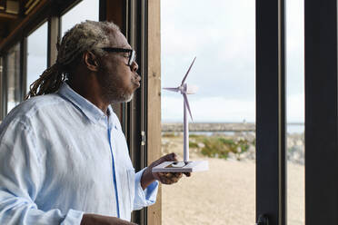 Engineer blowing on wind turbine model in cafe - ASGF04503