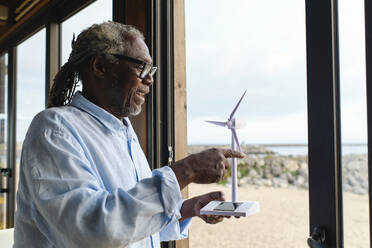 Glücklicher Ingenieur, der das Modell einer Windkraftanlage im Eingang eines Cafés berührt - ASGF04505