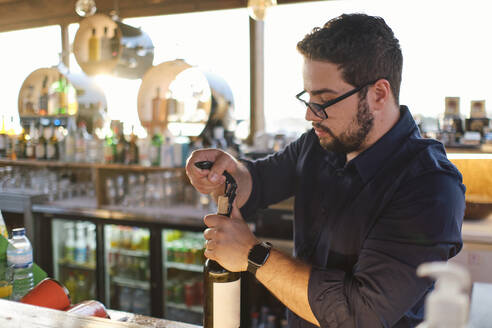 Junger Barkeeper öffnet eine Flasche Wein in einem Cafe - ASGF04520