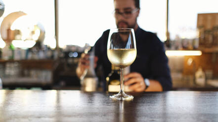 Glas Wein auf dem Tisch mit Barkeeper im Hintergrund - ASGF04523